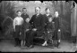 Vecpiebalgas ev.-lut. baznīcas ērģelnieks Jānis Kornets sēdus uz dekoratīva fotosalona sola ar sešu bērnu grupu. Diviem bērniem basas kājas. Uzņemts salonā uz apgleznota fona. Foto - Gustavs Žakerts